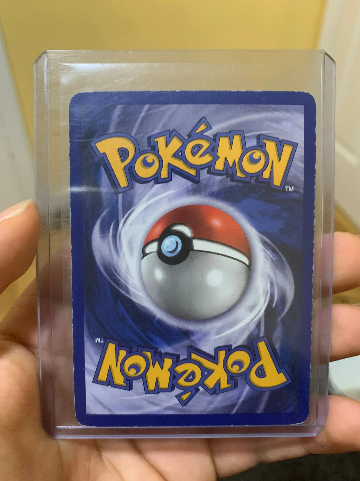 Hand holding a sleeved Pokémon card back with Poké Ball design, collectible trading card