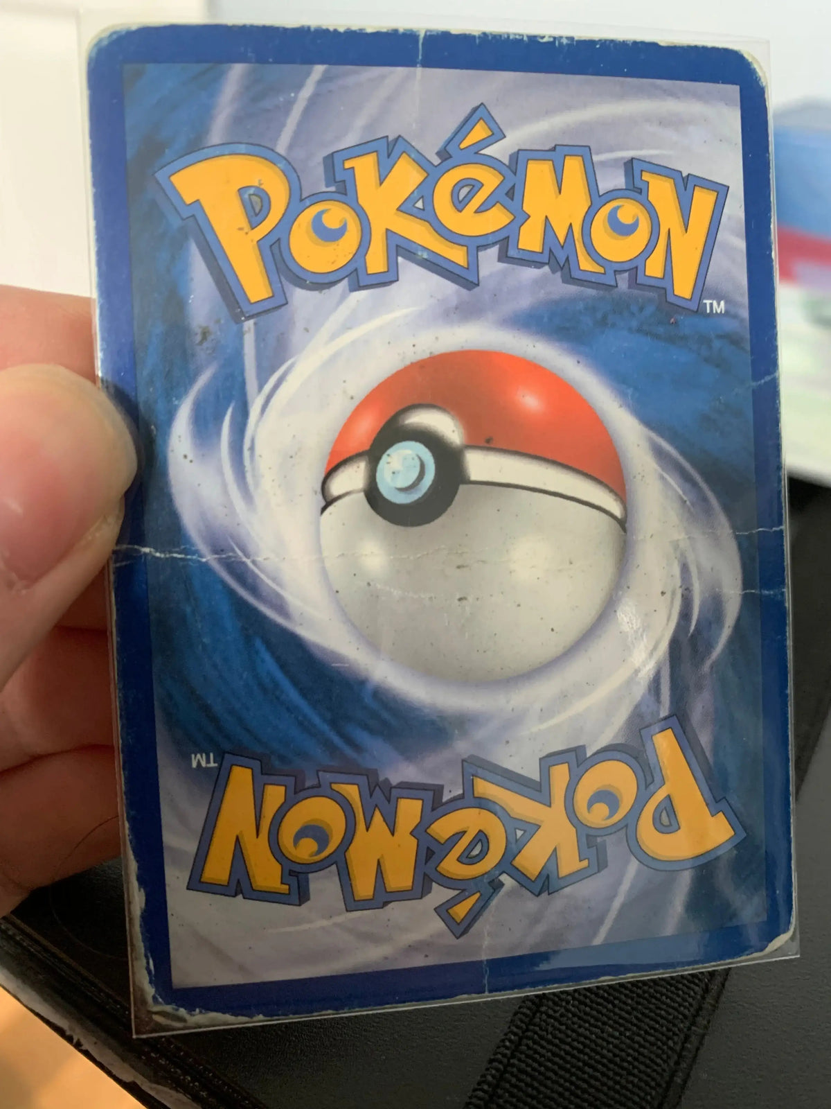 Worn Pokémon trading card back held by hand, collectible hobby shop product