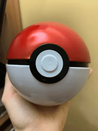 Hand holding a classic red and white Pokémon Poké Ball collectible toy from PTC Collectibles
